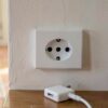 Prise italienne murale à trois trous alignés, avec un chargeur et un adaptateur posés dessous