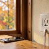 Prise canada à fentes plates sur le mur d'un chalet en automne, un smartphone posé sur la table en bois près de la fenêtre