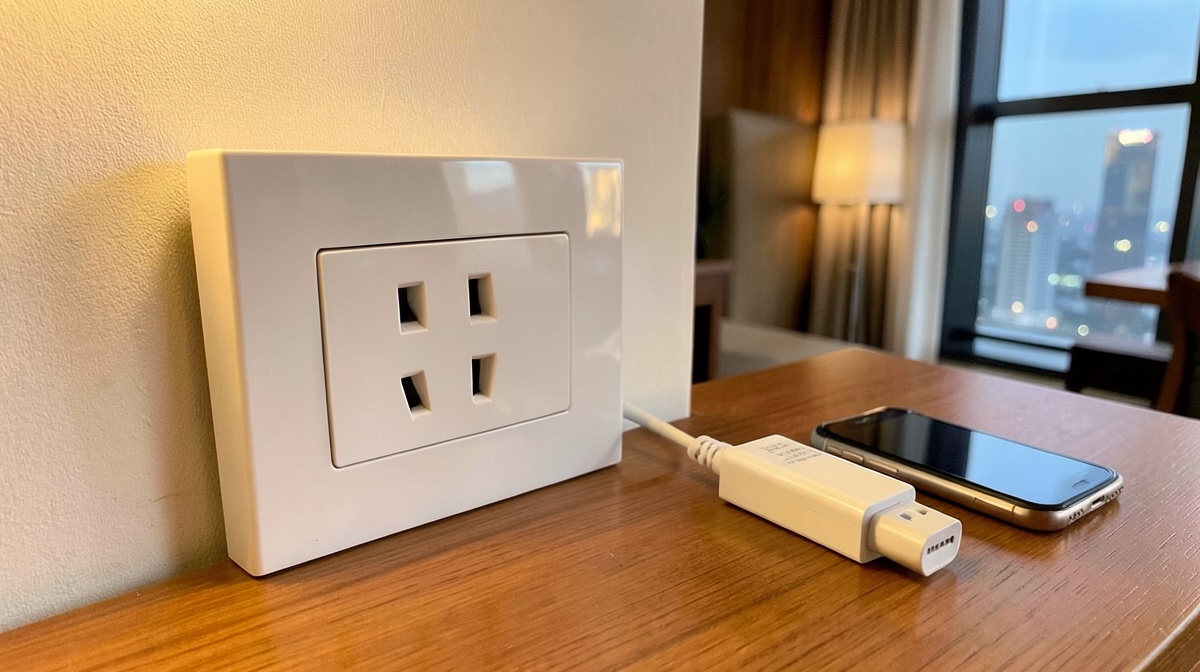 Prise chine murale blanche dans une chambre d'hôtel, avec un chargeur et un smartphone posés sur le bureau face à la ville