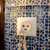 Prise Maroc : chargeur de téléphone branché sur une prise murale à deux trous ronds dans une chambre de riad au mur en zellige