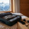 Prise suisse en voyage : valise ouverte dans un chalet face aux Alpes, adaptateur de voyage et smartphone posés sur la table de chevet