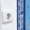 Prise Tunisie : prise murale ronde européenne sur un mur blanc à côté d'un volet bleu sculpté